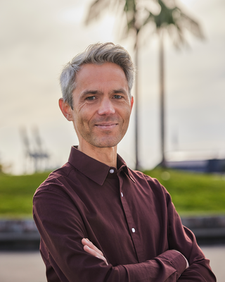 Ein Mann steht mit verschränkten Armen vor künstlichen Palmen