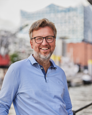 Ein Mann steht vor der Elbphilharmonie und lacht