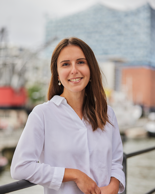Frau mit schulterlangen, braunen Haaren in einem weißem Hemd steht vor der Elbphilharmonie.